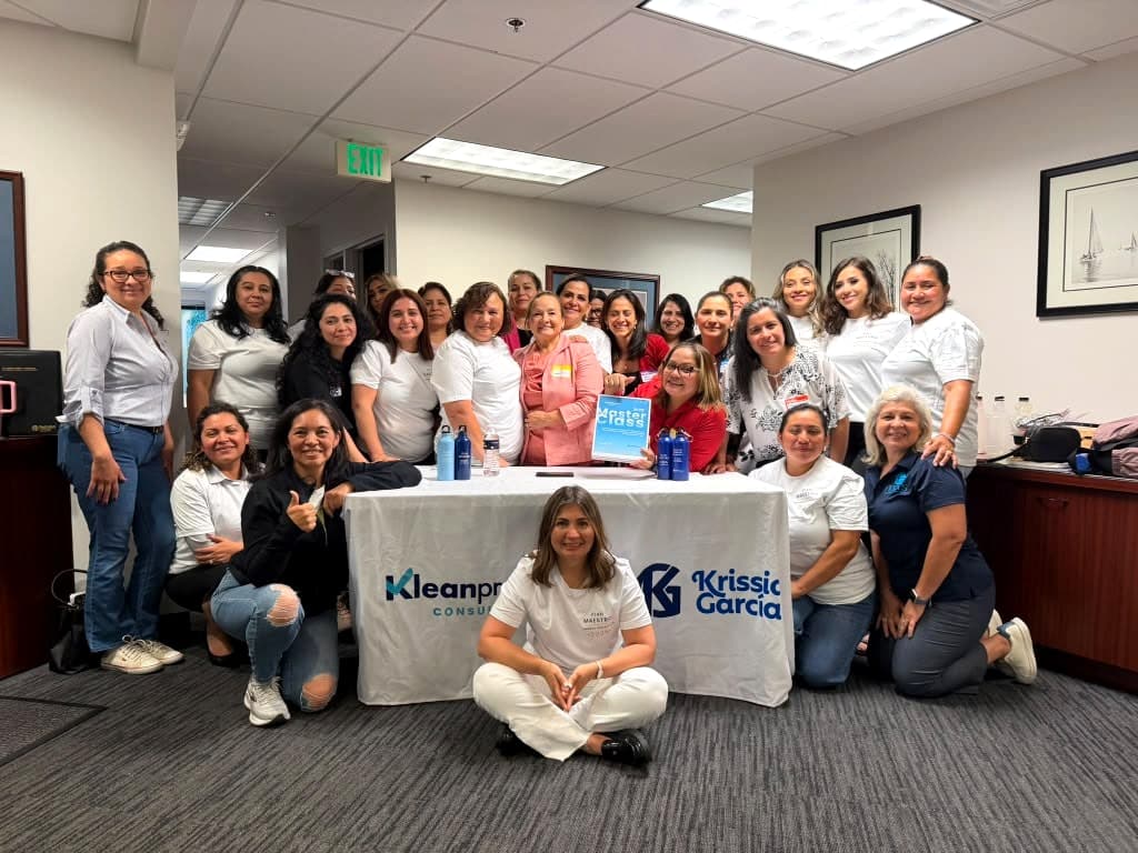 Grupo de dueñas de compañías de limpieza reunidas en una Master Class de Kleanpreneurs, junto a una mesa con la marca Kleanpreneurs Consulting y Krissia García